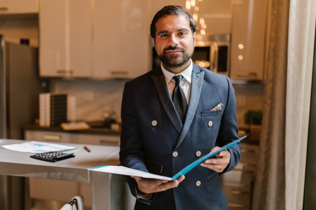 a-man-in-blue-suit-jacket-holding-blue-folder-8068727 Professional businessman in a suit holding a folder with a confident smile in a modern office.